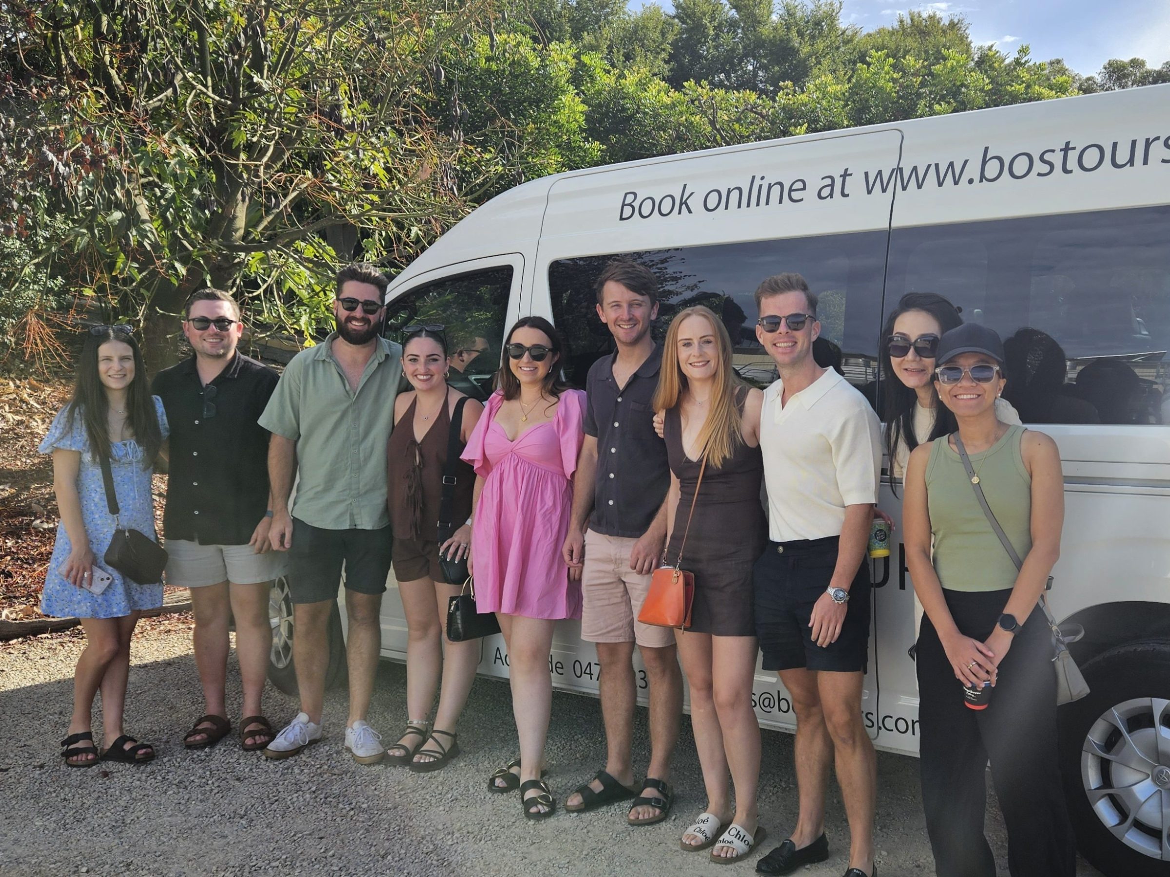Group of people posing in front of a tour van with 'Book online at www.bostours.com.au' printed on it.