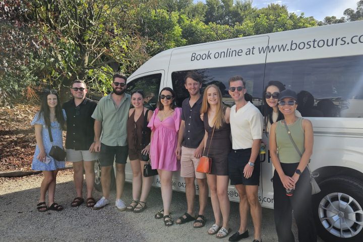 Group of people posing in front of a tour van with 'Book online at www.bostours.com.au' printed on it.