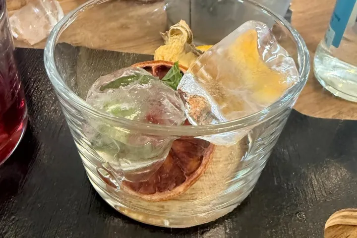 Glass with ice cubes, dried citrus, and mint on a wooden table.