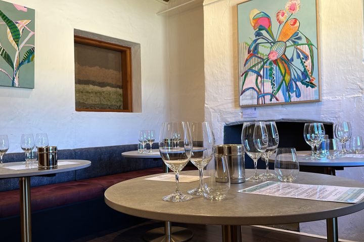 Cozy room with round tables, wine glasses, and colorful plant paintings on the wall.