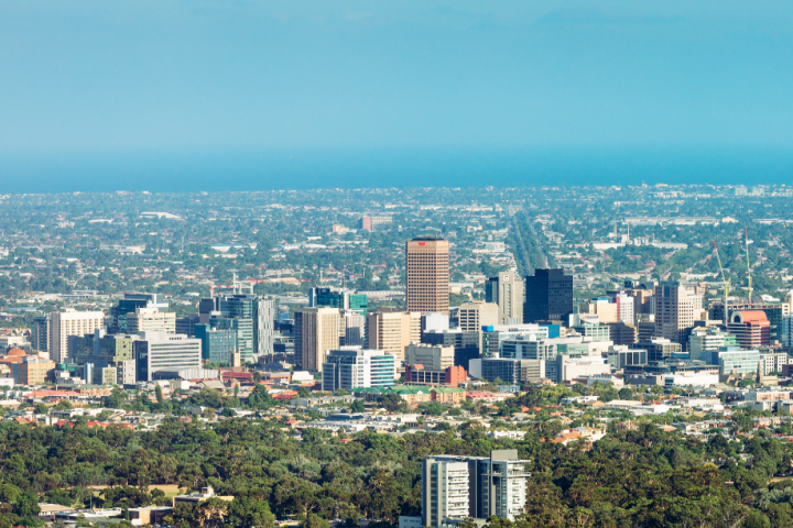 Skyline of a city with buildings, trees, and a blue sky, labeled 'Adelaide City'.