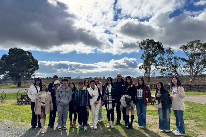 Group of people posing outside with trees and cloudy sky in the background.