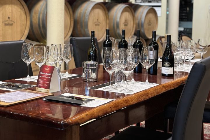 Wine tasting setup with glasses, bottles, and barrels in a cellar setting.