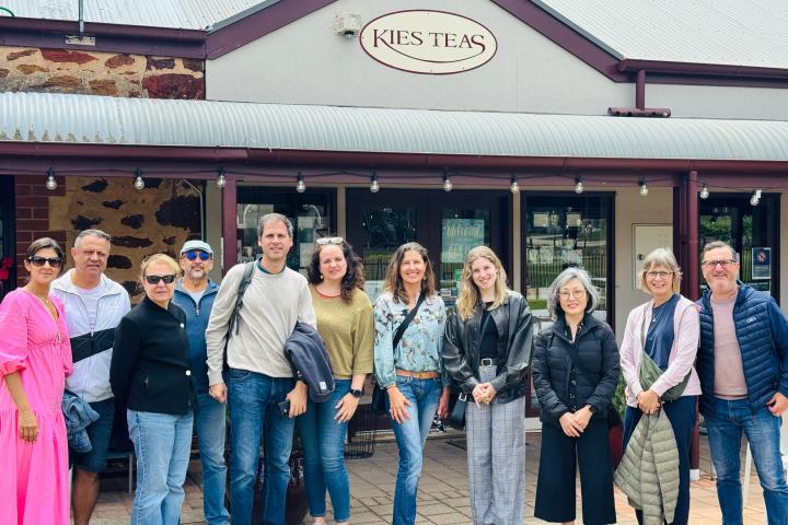 Group of people smiling in front of a building with 'Kies Teas' sign.