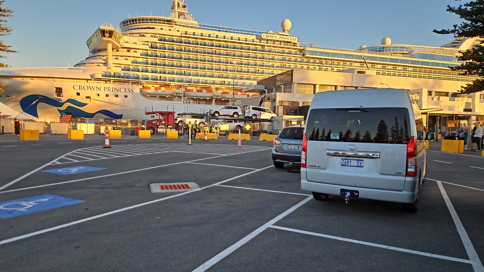 Cruise ship Crown Princess docked at port with cars and a van in the foreground parking lot.