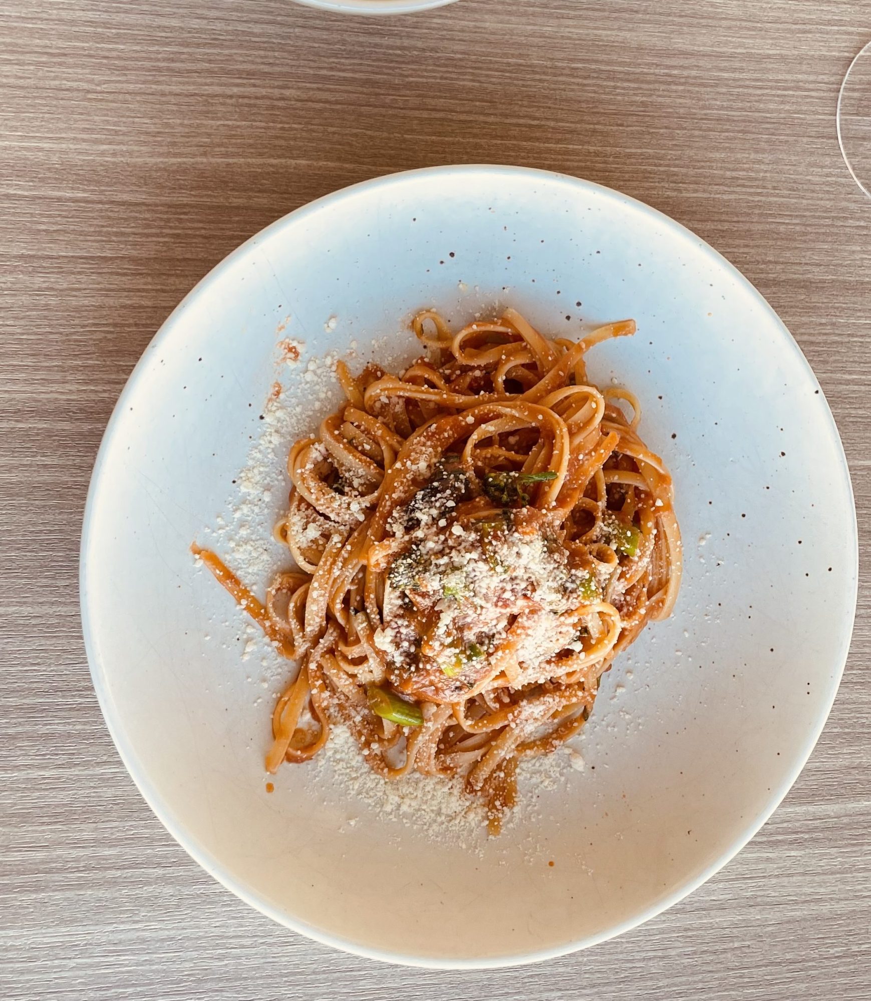 Plate of spaghetti with tomato sauce and cheese, fork and knife on napkin nearby.