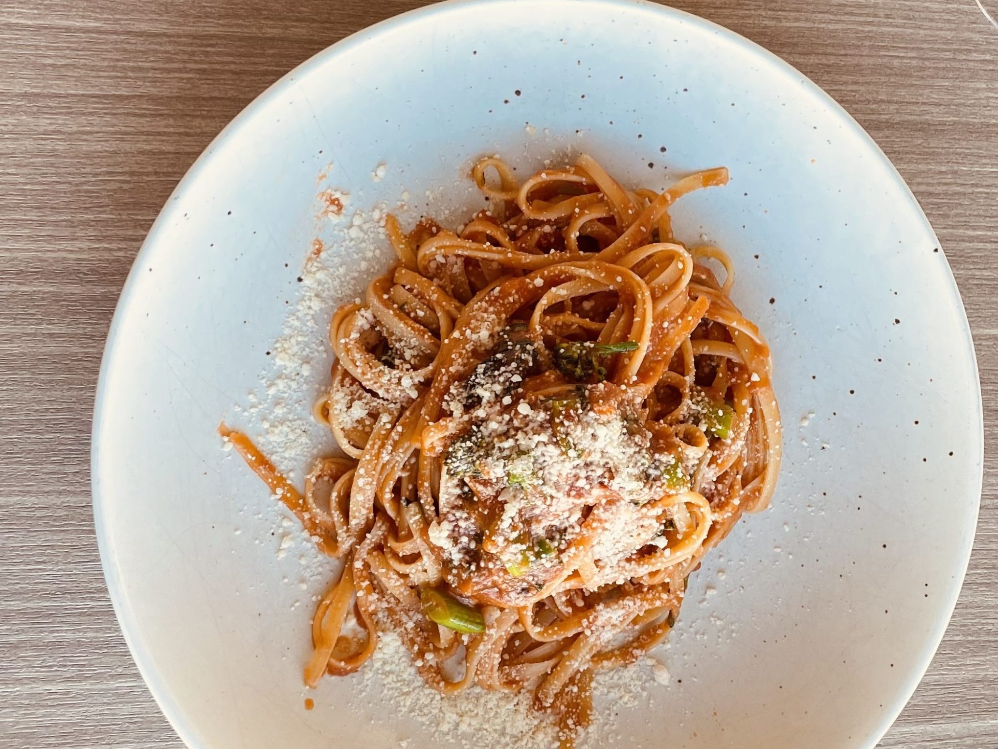 Plate of spaghetti with tomato sauce and cheese, fork and knife on napkin nearby.