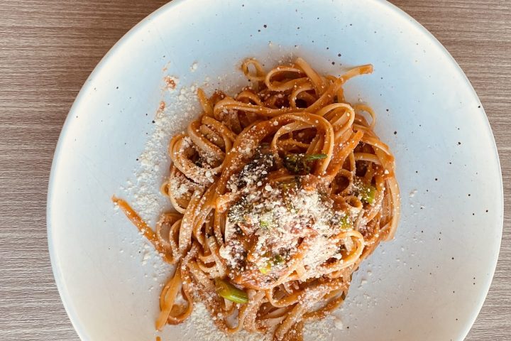 Plate of spaghetti with tomato sauce and cheese, fork and knife on napkin nearby.