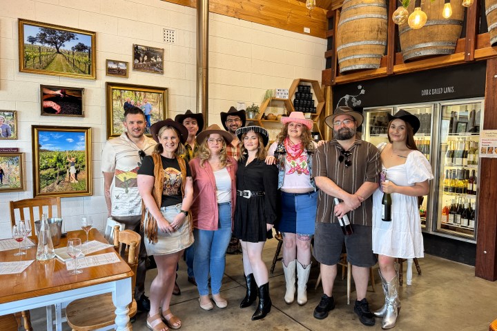 Group of people in cowboy hats and boots posing indoors near wine area.