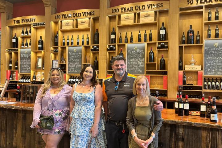 Group of four people smiling in front of a wine display with shelves labeled by vine age.