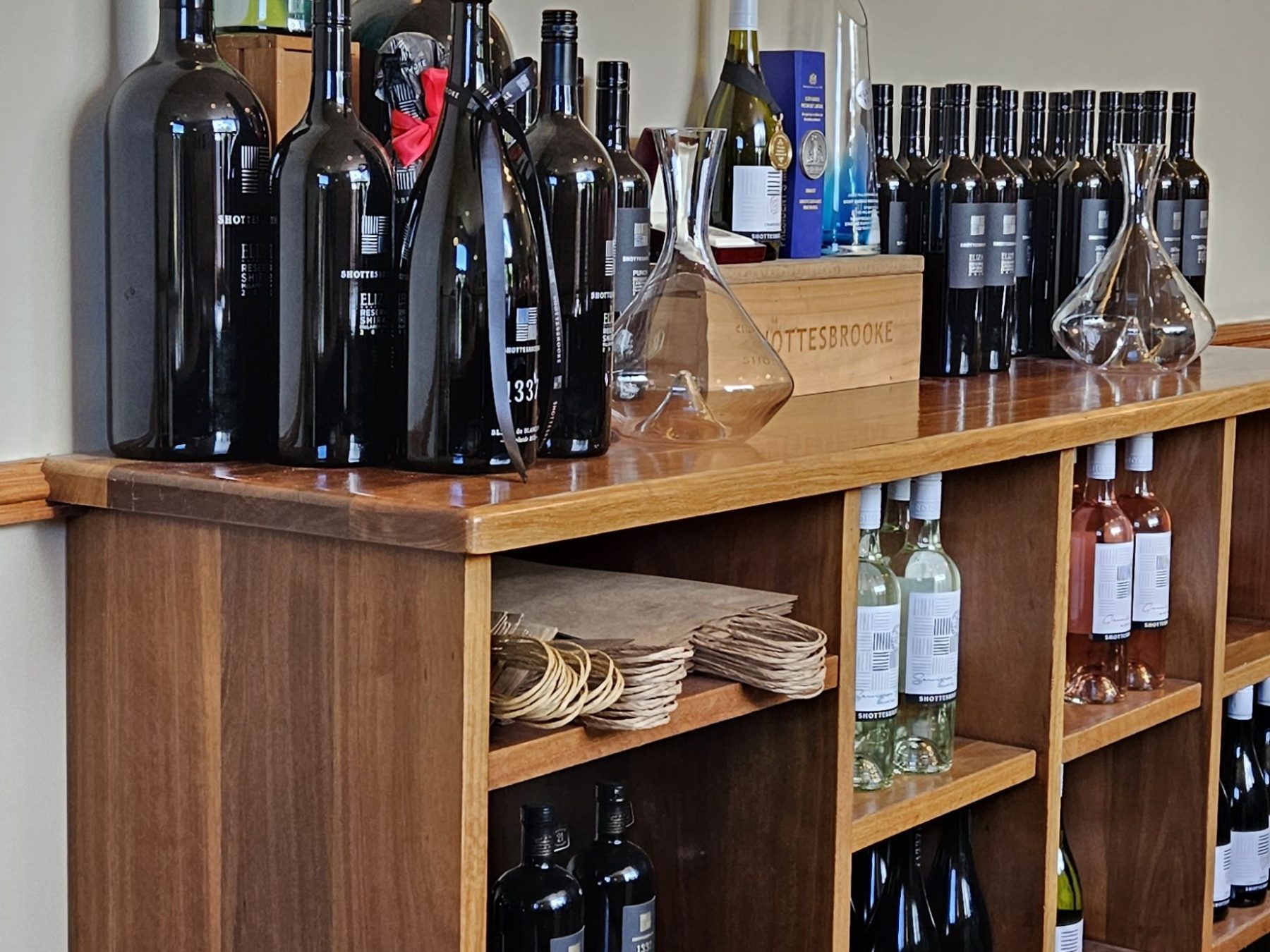 Wooden shelves displaying assorted wine bottles and decanters under a Shottesbrooke sign.
