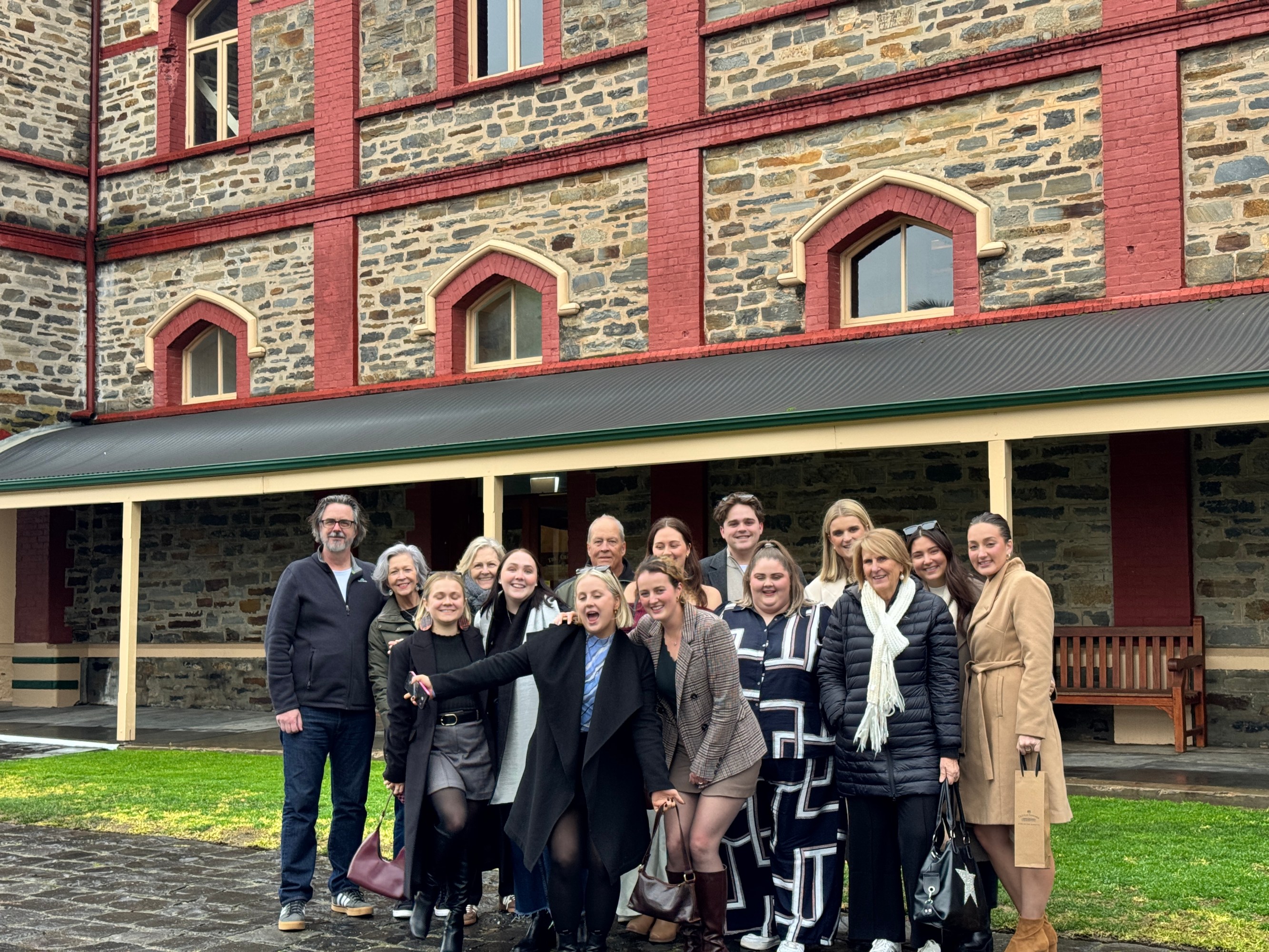 Group of people posing happily outside a large brick building.