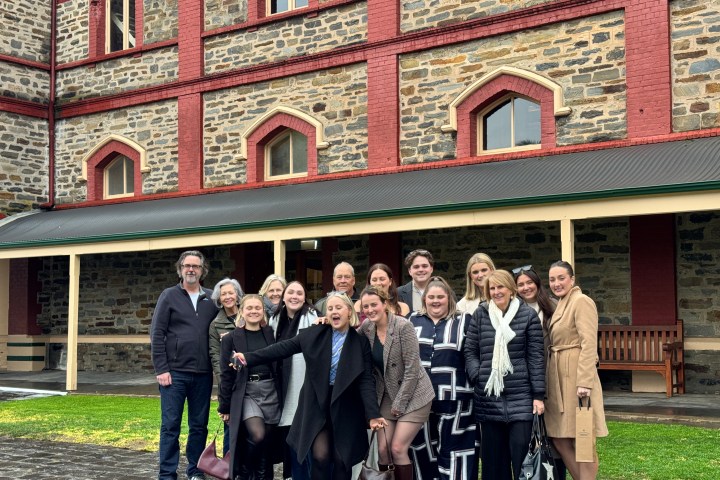 Group of people posing happily outside a large brick building.