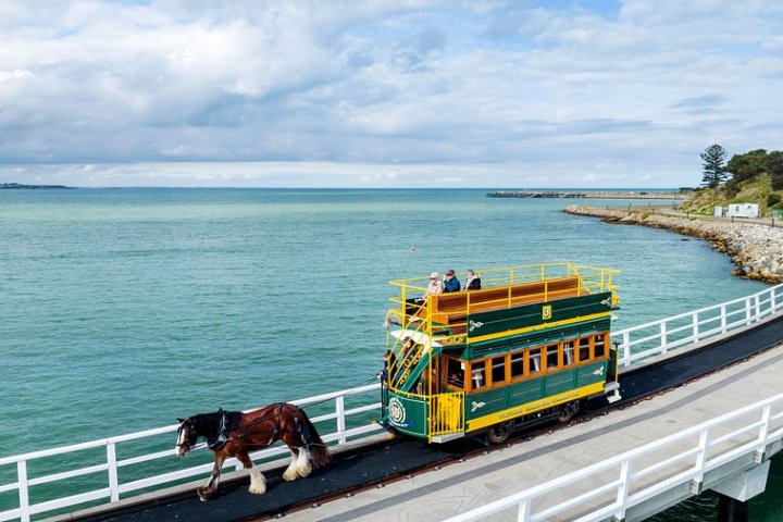 Horse-drawn tram crossing a bridge over scenic blue water with passengers on top deck.