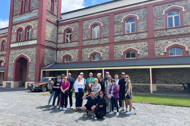 Group of people posing in front of a historic stone building with arched windows.