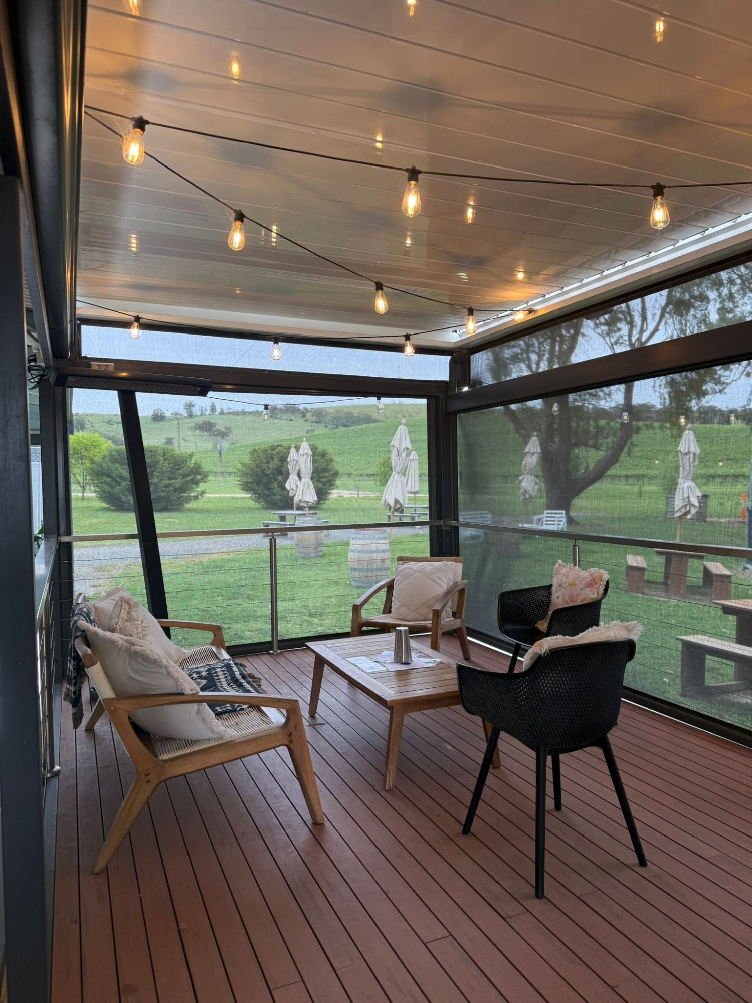 Covered patio with string lights, chairs, and table overlooking a green landscape.