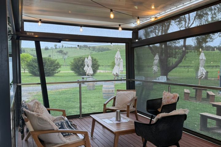 Covered patio with string lights, chairs, and table overlooking a green landscape.