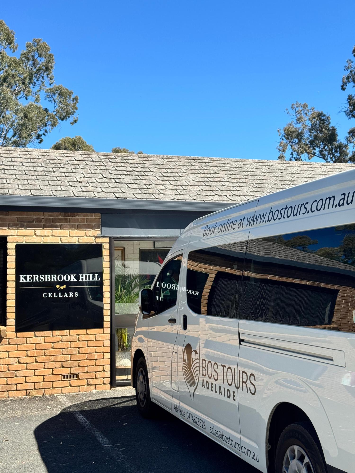 Van parked by Kersbrook Hill Cellars sign, clear blue sky and trees in background.