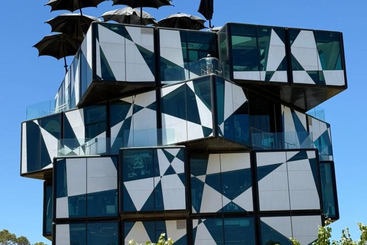 Modern geometric building with umbrellas on top and clear blue sky.