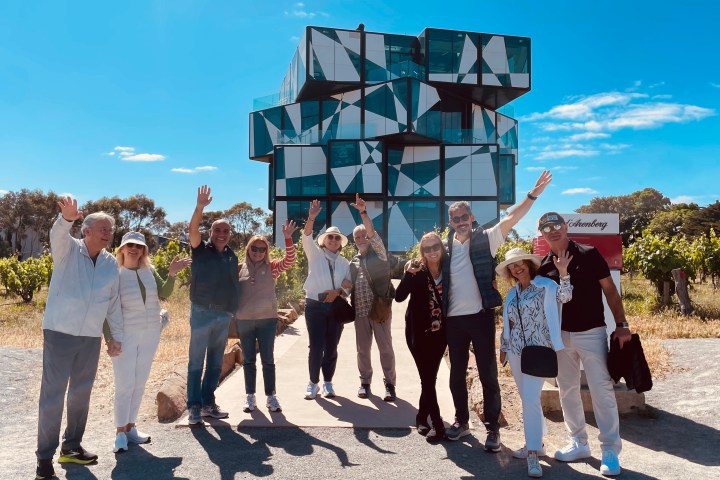 Group of people waving in front of a modern geometric building.