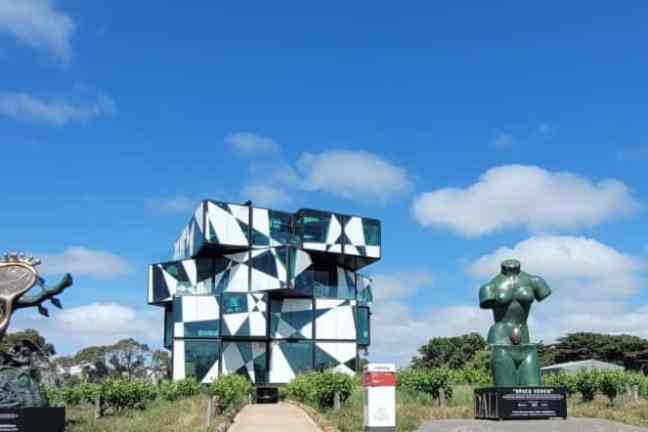 Modern building and three abstract sculptures under a blue sky with clouds.