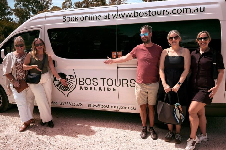 Group of five people posing in front of a tour van with a logo and website details.
