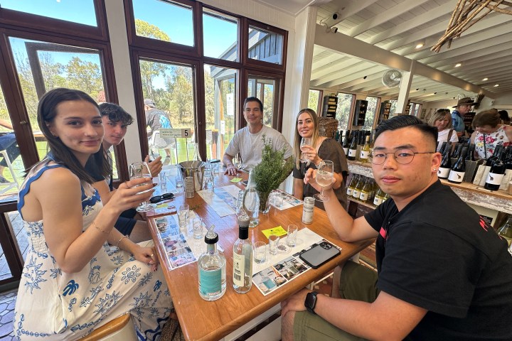 Group of five people enjoying wine at a wooden table in a bright room.