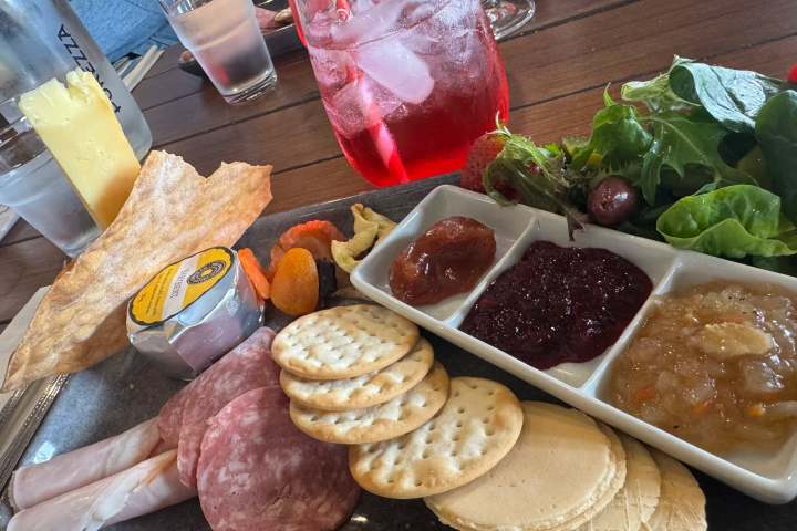 Charcuterie board with meats, crackers, spreads, salad, and a red drink on a table.