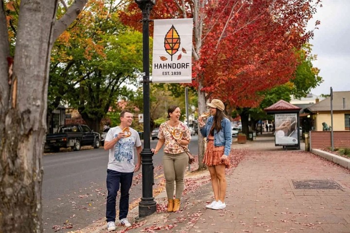 Three people eating ice cream under autumn leaves in a small town setting.